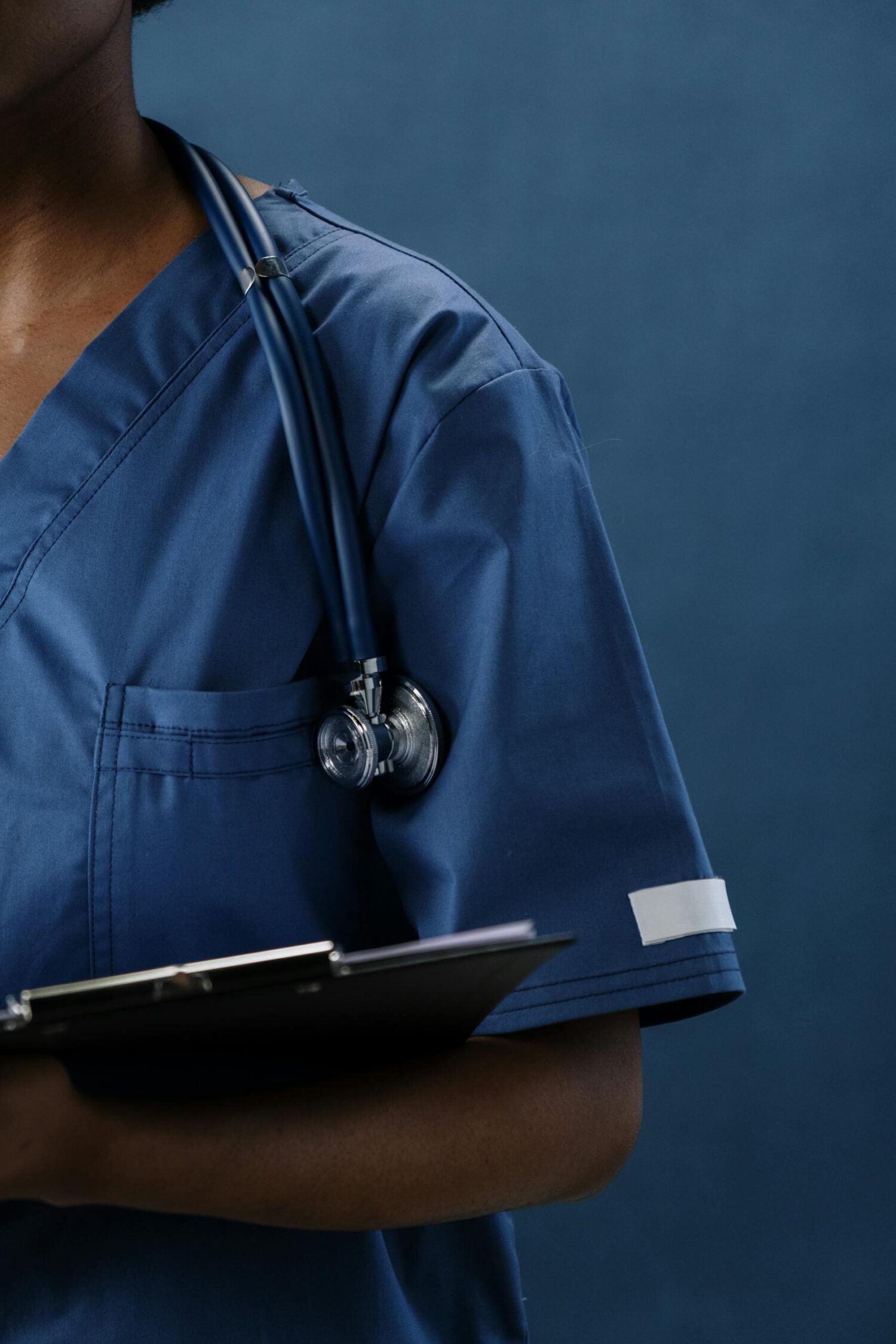 Close-up of a healthcare professional in blue scrubs with a stethoscope and clipboard.