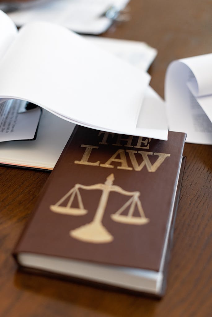 Close-up of a law book with scales icon on a wooden desk covered in papers.